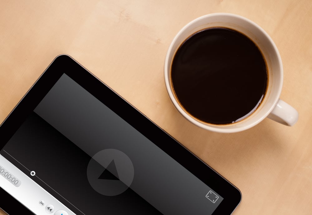 Workplace with tablet pc showing media player and a cup of coffee on a wooden work table close-up